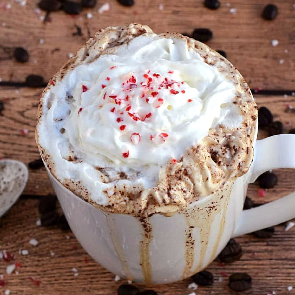 A coffee mug overflowing with coffee and whipped cream, and topped with crushed peppermint.