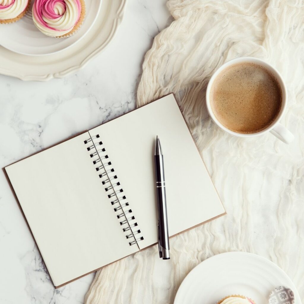 Blank journals and cup of coffee with cupcakes in the left corner.